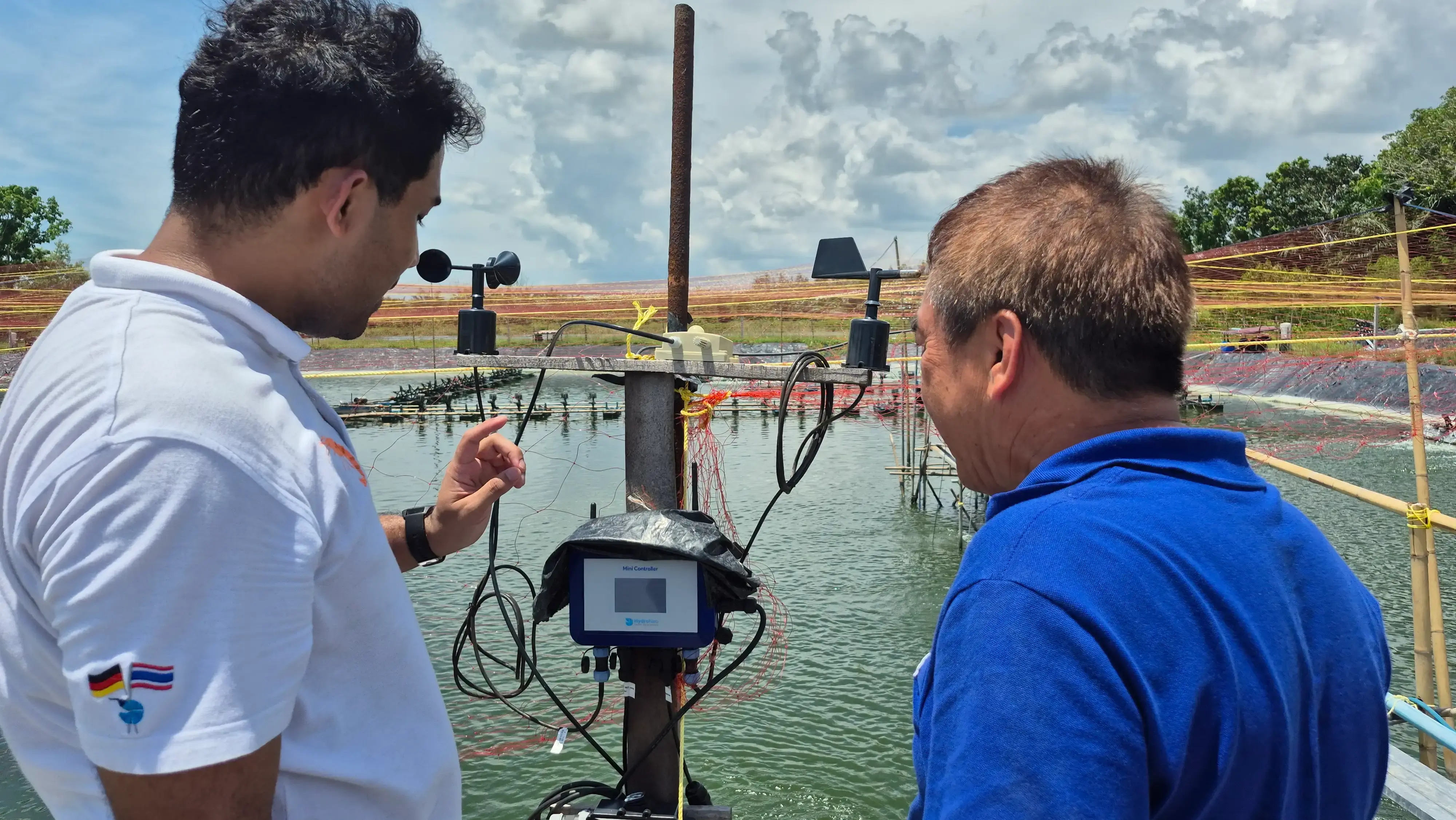 Two people inspecting water quality monitoring equipment by HydroNeo at the edge of a shrimp pond, with sensors and control devices installed.
